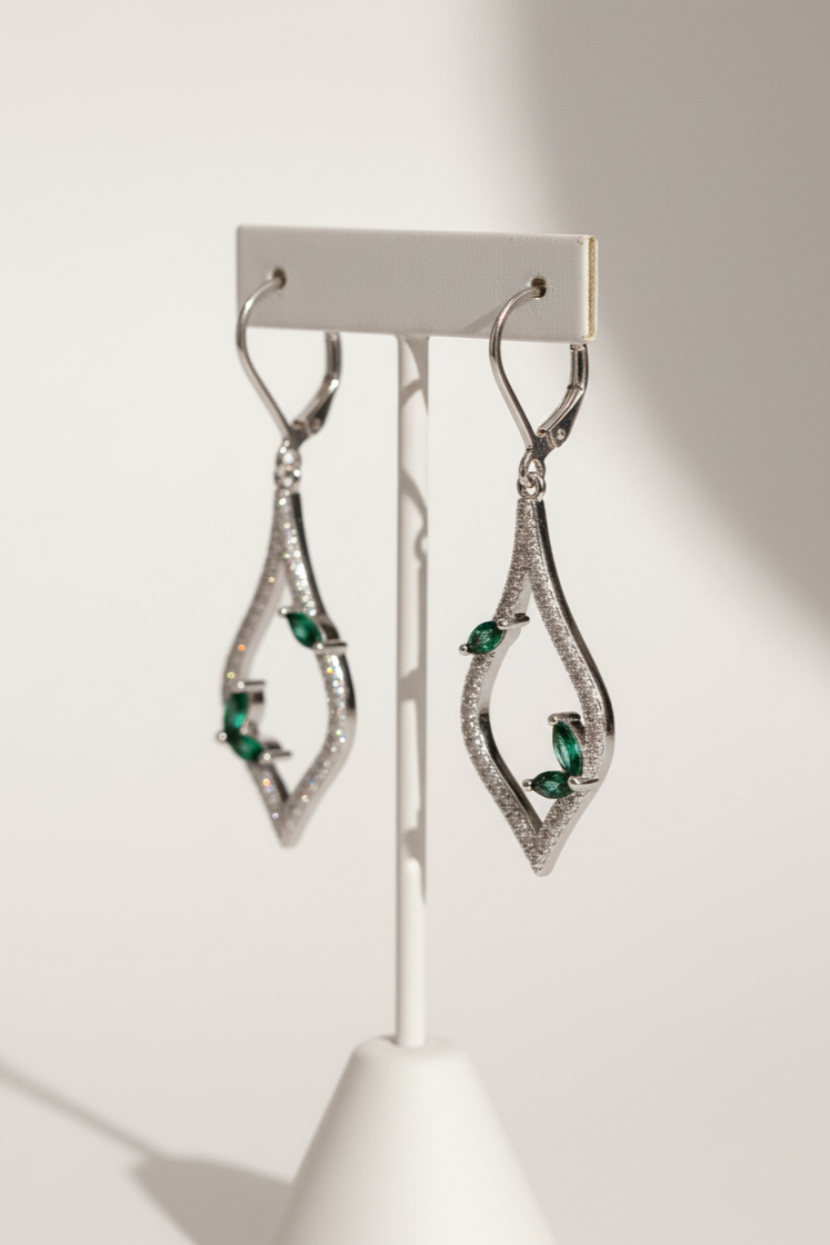 Pair of silver earrings with green gemstones on a white stand against a light gray background