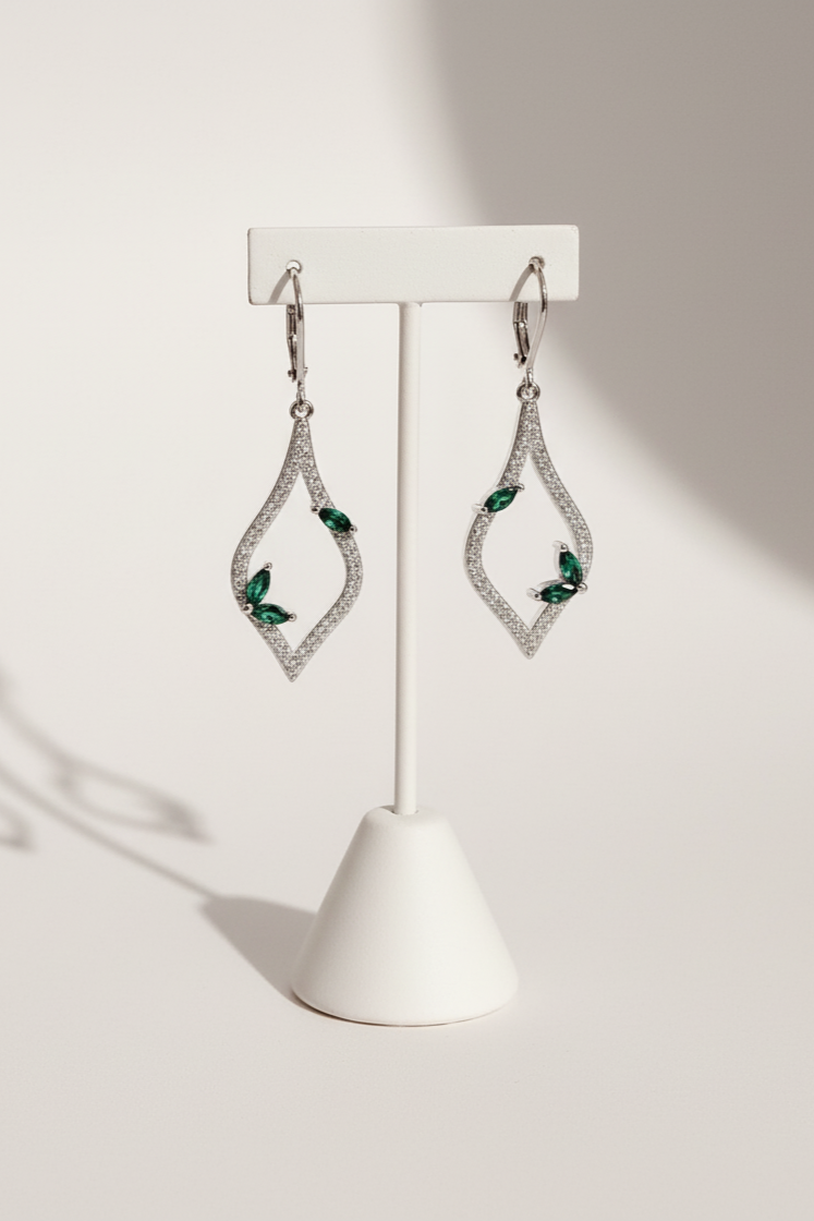 Pair of diamond and emerald earrings on a white stand against a light background